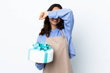 Pasta şefi, izole edilmiş beyaz arka plan üzerinde büyük bir pasta tutuyor. Gözleri elleriyle kaplıyor.