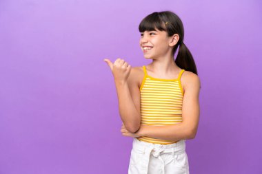 Mor arka planda izole edilmiş küçük beyaz çocuk bir ürünü sunmak için kenarı işaret ediyor.