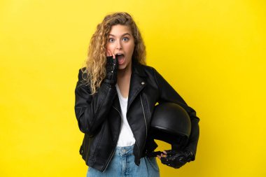 Motosiklet kasklı genç sarışın kadın sarı arka planda izole edilmiş, şaşırmış ve şok olmuş bir yüz ifadesi var.