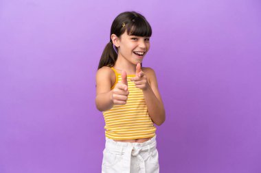 Mor arka planda izole edilmiş küçük beyaz çocuk şaşırmış ve ön tarafı işaret ediyor.