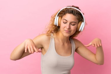 Genç sarışın kadın pembe arka planda izole edilmiş müzik ve dans dinliyor.