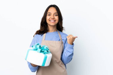 Pasta şefi izole edilmiş beyaz arka planda büyük bir pasta tutuyor. Baş parmakları havada ve gülümsüyor.