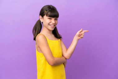 Mor arka planda izole edilmiş küçük beyaz çocuk, parmağıyla kenarı işaret ediyor.