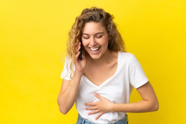 Sarı arka planda izole edilmiş cep telefonu kullanan genç sarışın kadın çok gülümsüyor.