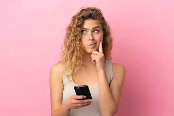 用手机和思维隔离在粉色背景下的年轻金发女人 — 图库照片
