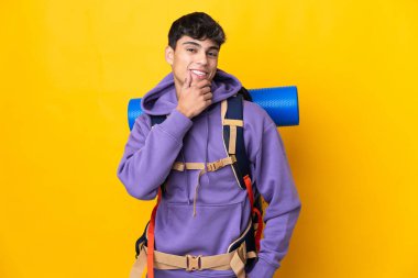 Sarı arka plan üzerinde büyük bir sırt çantası olan genç dağcı mutlu ve gülümsüyor.