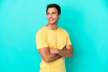 İzole edilmiş mavi arka planda kolları bağlı ve mutlu beyaz yakışıklı bir adam.