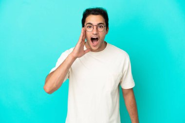 İzole edilmiş mavi arka planda beyaz yakışıklı adam ağzı açık bağırıyor.
