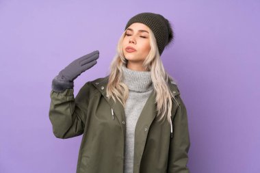 Kışlık şapkalı genç sarışın kız izole edilmiş mor arka plan ve yorgun ve hasta bir yüz ifadesi var.