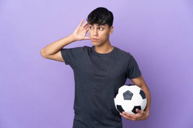 Genç futbolcu, izole edilmiş mor arka planda elini kulağına koyarak bir şeyler dinliyor.