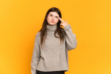 Genç Ukraynalı kız sarı arka planda izole edilmiş intihar jesti yapmada sorun yaşıyor.