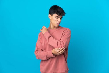 Genç adam mavi arka planda, dirseğinde ağrı var.