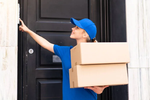 Young delivery woman at outdoors holding boxes and ringing the bell