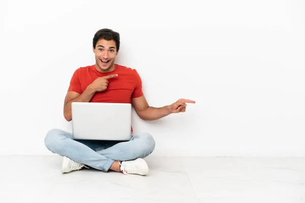 Homem Bonito Caucasiano Com Laptop Sentado Chão Surpreso Apontando Lado — Fotografia de Stock