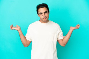 Kafkasyalı yakışıklı adam soyutlanmış mavi arka planda kuşkuları varken el kaldırıyor.