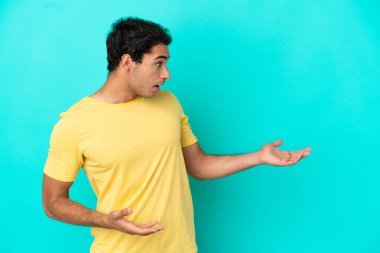 Kafkasyalı yakışıklı bir adam mavi arka planda, sürpriz bir ifadeyle yan yana bakarken.