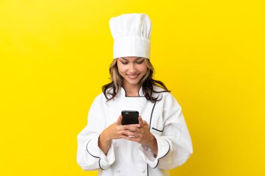 Sarı arka planda izole edilmiş genç bir Rus şef kız cep telefonuyla mesaj gönderiyor.