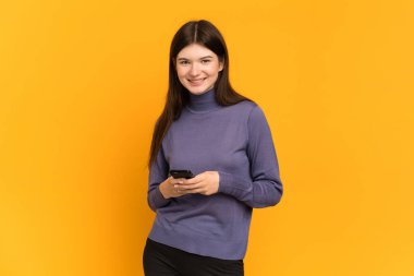 Sarı arka planda izole edilmiş genç Ukraynalı kız cep telefonuyla mesaj gönderiyor.