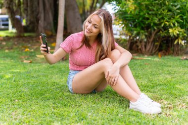 Açık havada genç ve güzel bir kadın mutlu bir ifadeyle cep telefonu kullanıyor.