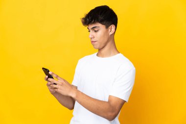 Sarı arka plan izole edilmiş genç adam cep telefonuyla bir mesaj ya da e-posta gönderiyor