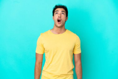 Kafkasyalı yakışıklı adam mavi arka plan üzerinde yukarı bakıyor ve şaşırmış bir ifadeyle