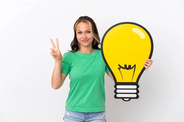 Teenager Russian Girl Isolated Blue Background Holding Bulb Icon Celebrating — Stock Photo, Image