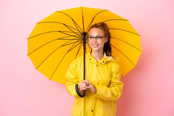 ティーンロシアの女の子ともにレインプルーフコートと傘隔離上のピンクの背景見に側と笑顔 — ストック写真