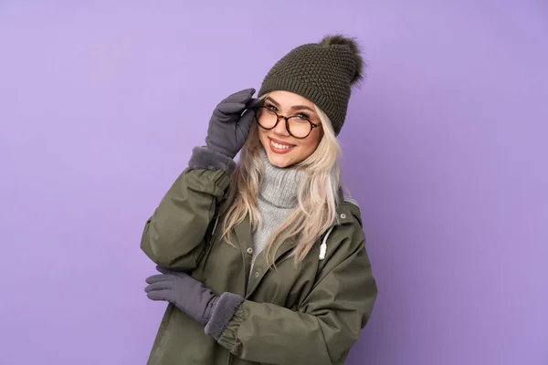 年轻的金发女郎 头戴冬帽 背景是紫色的 戴着眼镜 快乐极了 — 图库照片