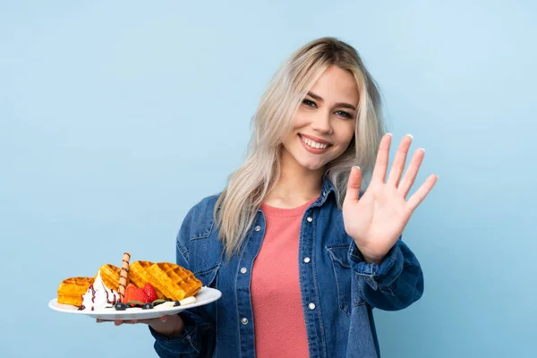 Tiener Meisje Houden Wafels Geïsoleerde Blauwe Achtergrond Salueren Met Hand — Stockfoto