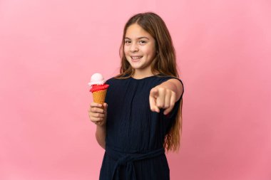 Kornet dondurması ile izole edilmiş pembe arka planı olan çocuk mutlu bir ifadeyle önü işaret ediyor.