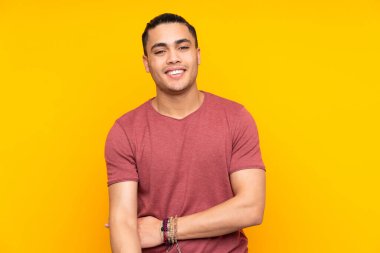 Sarı arka planda izole edilmiş Asyalı yakışıklı bir adam bir ürün sunmak ve bir şeyler fısıldamak için kenarı işaret ediyor.