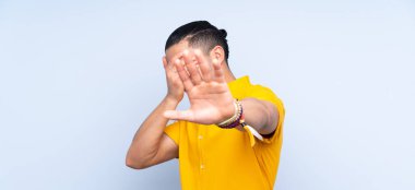 Asyalı yakışıklı adam soyutlanmış arka planda jest yapıyor ve yüzünü kapatıyor.