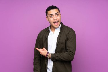 Asyalı yakışıklı adam mavi arka planda mahsur kalmış, şaşırmış ve işaret ediyor.