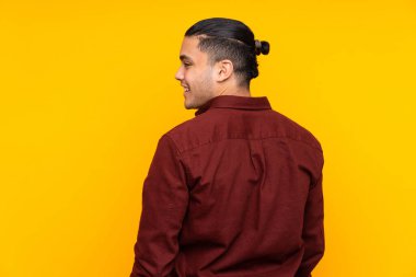 Asyalı yakışıklı adam sarı arka planda izole edilmiş. Sessiz bir jest işareti var. Parmağını ağzına sok.