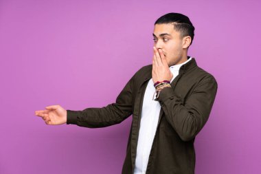 Asyalı yakışıklı adam mavi arka planda izole edilmiş sürpriz bir ifadeyle işaret ederken