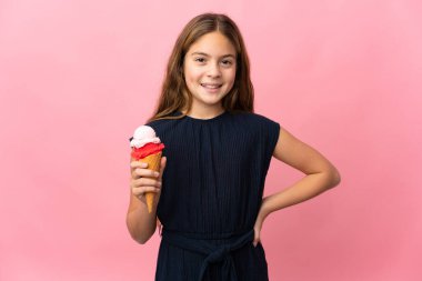 Kornet dondurması olan çocuk pembe arka planda kolları kalçasında ve gülümsüyor.