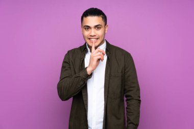 Asyalı yakışıklı adam mavi arka planda izole edilmiş. Sessiz bir jest işareti var. Parmağını ağzına sok.