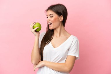 Pembe arka planda izole edilmiş beyaz bir kadın elma yiyor.