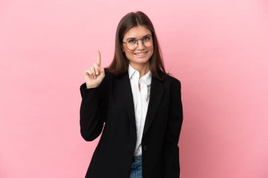 Genç beyaz kadın pembe arka planda izole edildi ve en iyinin işareti olarak parmağını kaldırdı.