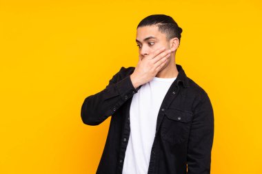 Asyalı yakışıklı adam sarı arka planda tek başına ağzını eliyle kapatıyor.