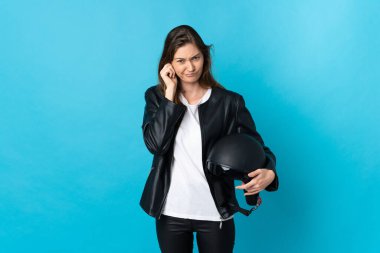 Mavi arka planda izole edilmiş motosiklet kaskı tutan genç İrlandalı kadın hayal kırıklığına uğramış ve kulaklarını kapatmış.