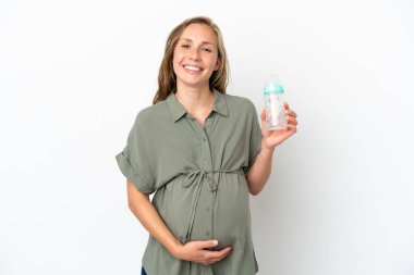 Beyaz arka planda izole edilmiş genç beyaz kadın hamile ve elinde bir beslenme şişesi var.