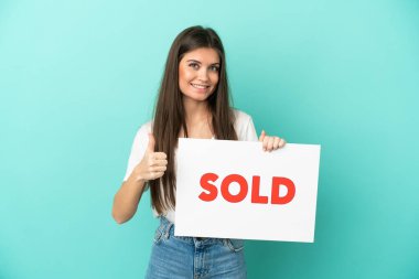 Kafkasyalı genç bir kadın mavi arka planda izole edilmiş. Elinde başparmağıyla satılan bir pankart var.