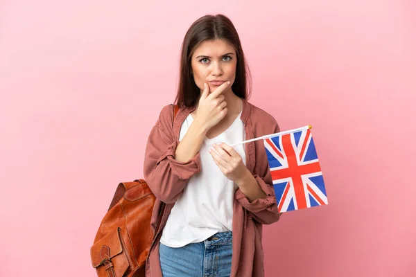 Young caucasian woman holding an United Kingdom flag isolated on pink background thinking