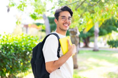 Genç bir öğrenci dışarıda elinde mutlu bir ifadeyle bir defter tutuyor.
