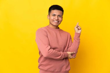 Young Ecuadorian man isolated on yellow background happy and pointing up
