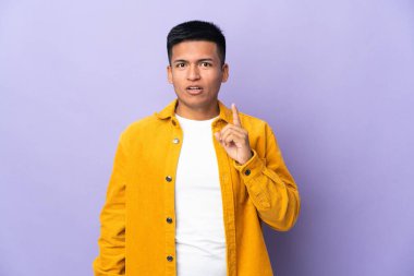 Genç Ekvador 'lu adam mor arka planda izole edilmiş. Çözümü, parmağını kaldırarak anlamaya çalışıyor.