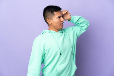 Young Ecuadorian man isolated on purple background with surprise expression while looking side