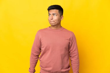 Genç Ekvadorlu adam sarı arka planda izole edilmiş, yukarı bakarken şüpheleri var.