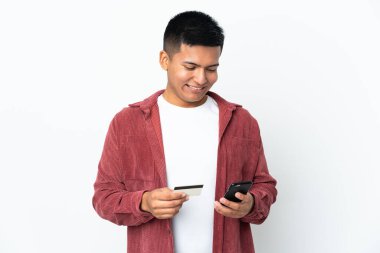 Genç Ekvadorlu adam beyaz arka planda izole edilmiş cep telefonuyla kredi kartıyla alışveriş yapıyor.